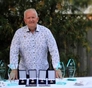 Man standing behind table full of awards